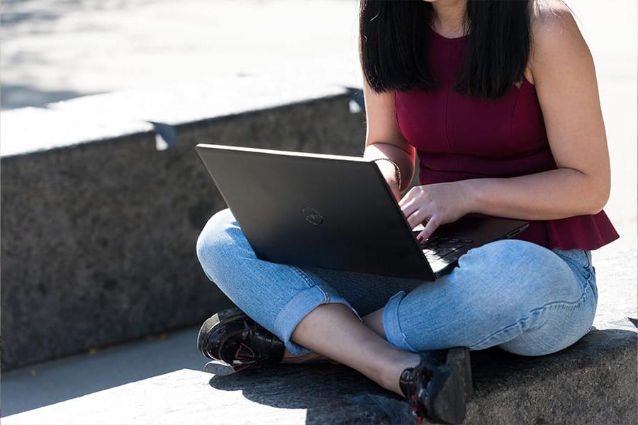 Student types on laptop outside.